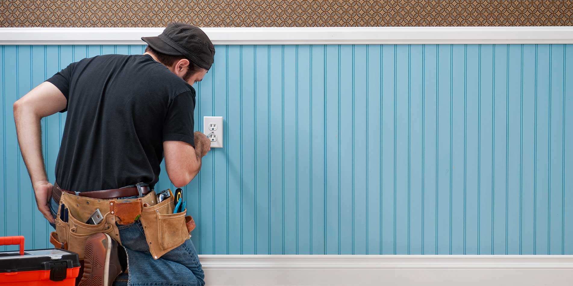 A man with a tool belt is looking at the wall.